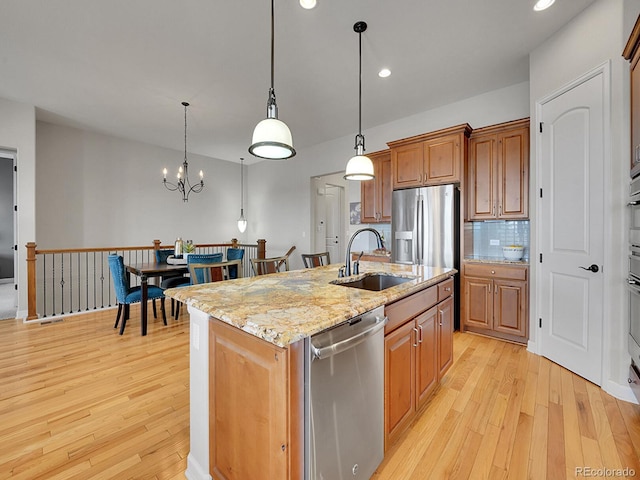 kitchen with sink, light hardwood / wood-style flooring, hanging light fixtures, stainless steel appliances, and an island with sink