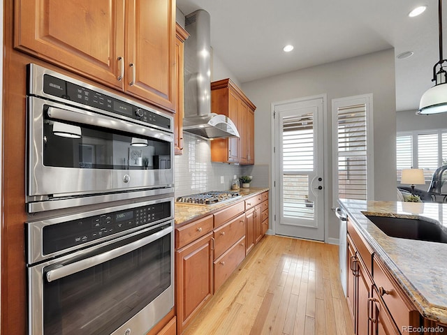 kitchen featuring sink, pendant lighting, stainless steel appliances, range hood, and backsplash