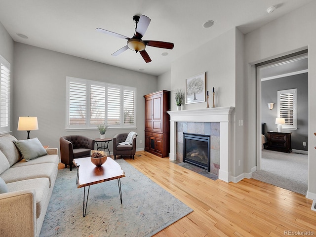 living room featuring ceiling fan, a healthy amount of sunlight, a fireplace, and light hardwood / wood-style flooring