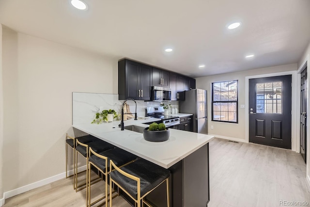 kitchen featuring stainless steel appliances, a sink, a kitchen breakfast bar, light wood-type flooring, and decorative backsplash