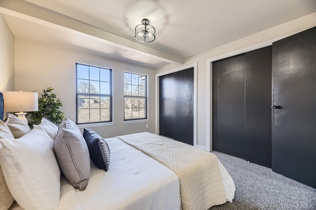 carpeted bedroom with multiple closets and beam ceiling