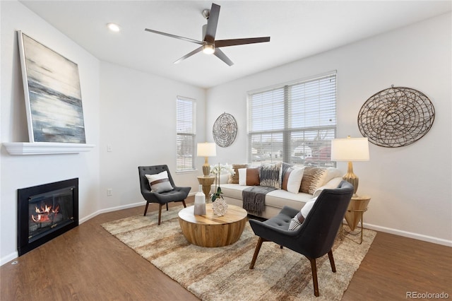 living room featuring baseboards, wood finished floors, a glass covered fireplace, and ceiling fan