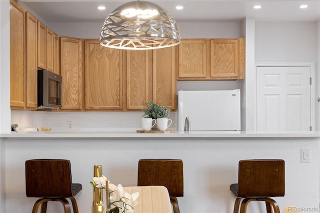 kitchen with stainless steel microwave, freestanding refrigerator, light countertops, and recessed lighting