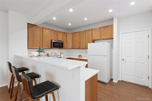 kitchen featuring a breakfast bar, white appliances, light wood finished floors, light countertops, and a peninsula
