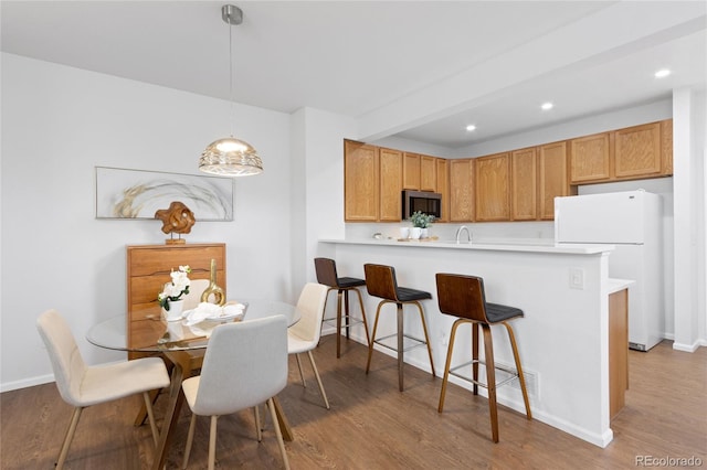 kitchen with light wood finished floors, stainless steel microwave, freestanding refrigerator, a peninsula, and a breakfast bar area
