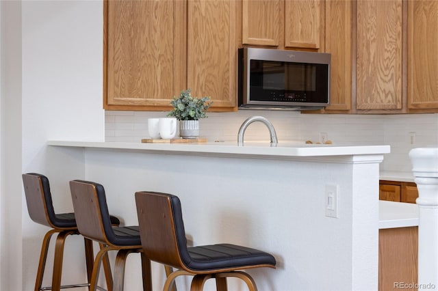 kitchen with a kitchen bar, stainless steel microwave, decorative backsplash, and light countertops
