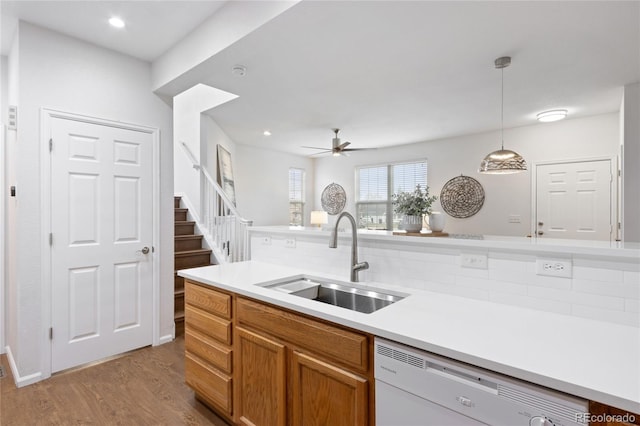 kitchen with brown cabinets, dishwasher, wood finished floors, a sink, and decorative light fixtures