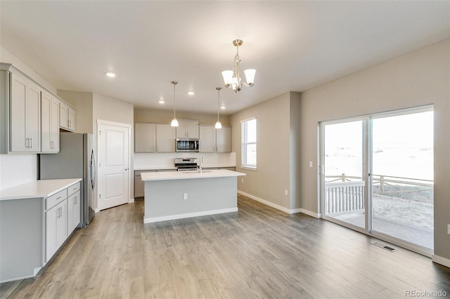 kitchen featuring gray cabinetry, a kitchen island with sink, hanging light fixtures, a notable chandelier, and stainless steel appliances