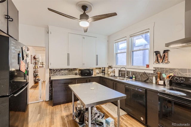 kitchen with tasteful backsplash, white cabinetry, sink, black appliances, and wall chimney range hood