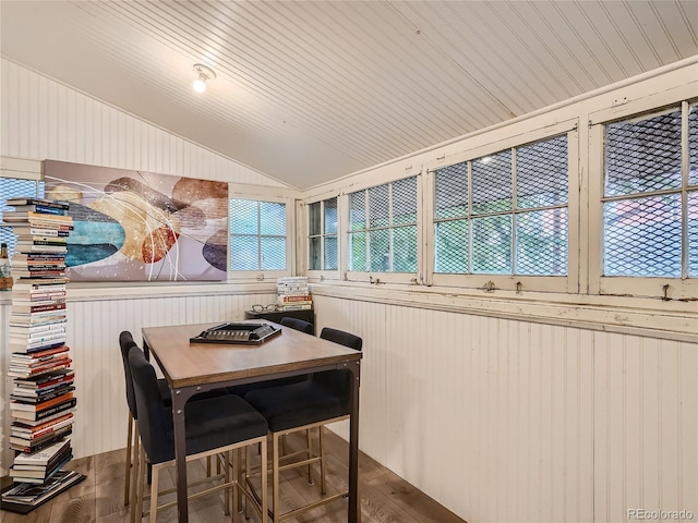 dining area with hardwood / wood-style flooring, vaulted ceiling, and wood walls