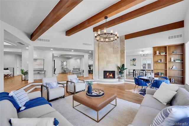 living room featuring beam ceiling, a premium fireplace, light hardwood / wood-style floors, and an inviting chandelier