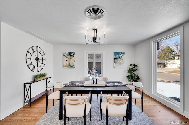 dining room with a textured ceiling, a chandelier, and light hardwood / wood-style floors