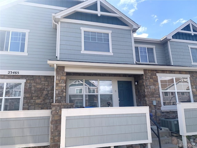 view of front of house with board and batten siding, stone siding, and central air condition unit