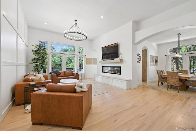 17912 Loverly Way, Monument, CO 80132 - living area with an inviting chandelier, a glass covered fireplace, baseboards, arched walkways, and light wood-style flooring