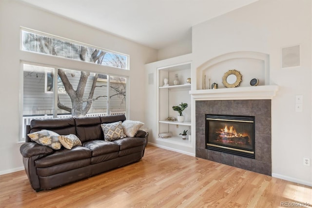 living room featuring a tile fireplace, hardwood / wood-style floors, and built in shelves