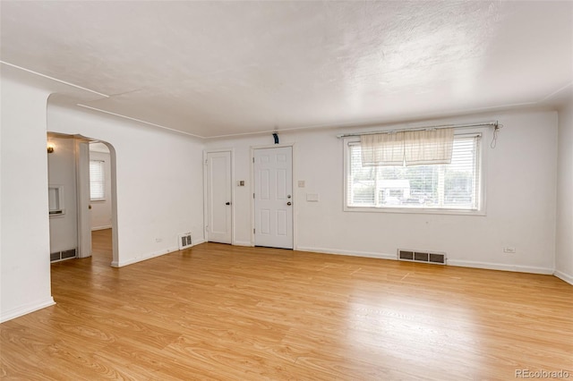 unfurnished living room with visible vents, arched walkways, and light wood-style flooring