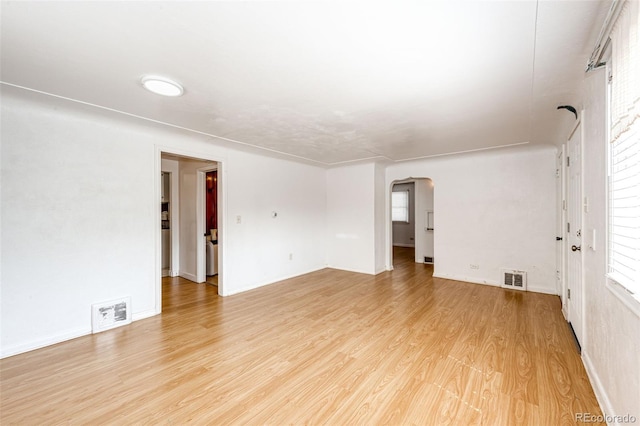 spare room featuring light wood-style floors, arched walkways, plenty of natural light, and visible vents