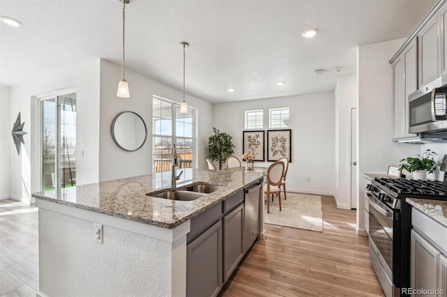 kitchen with gray cabinets, a sink, pendant lighting, stainless steel appliances, and light wood-style floors