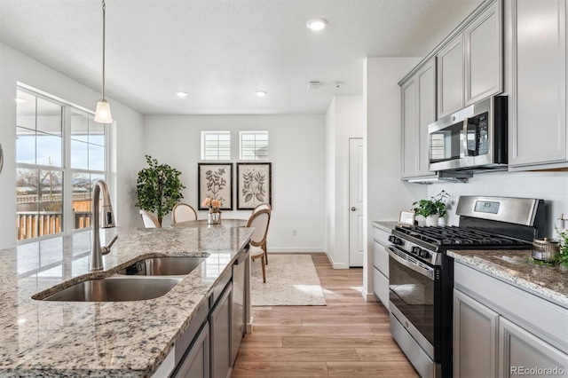 kitchen with light wood finished floors, light stone countertops, stainless steel appliances, a sink, and gray cabinets