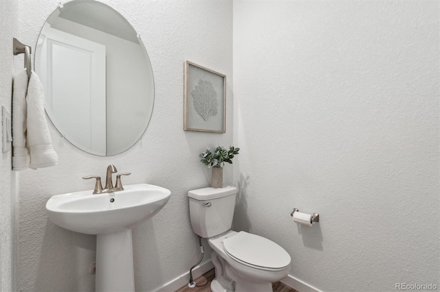 half bath featuring baseboards, toilet, wood finished floors, a sink, and a textured wall