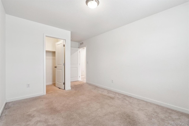 unfurnished bedroom with a closet, light carpet, a walk in closet, baseboards, and visible vents