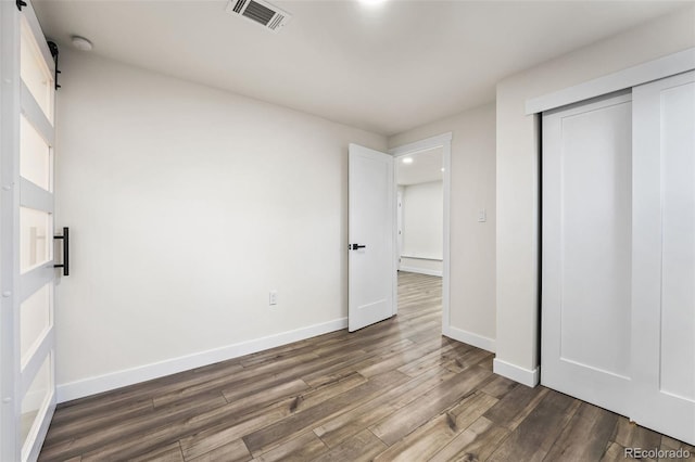 unfurnished bedroom featuring a barn door, dark wood-type flooring, and a closet