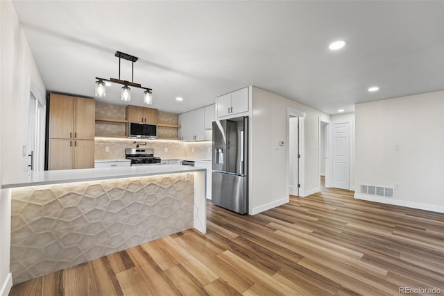 kitchen with kitchen peninsula, appliances with stainless steel finishes, white cabinets, light hardwood / wood-style floors, and hanging light fixtures