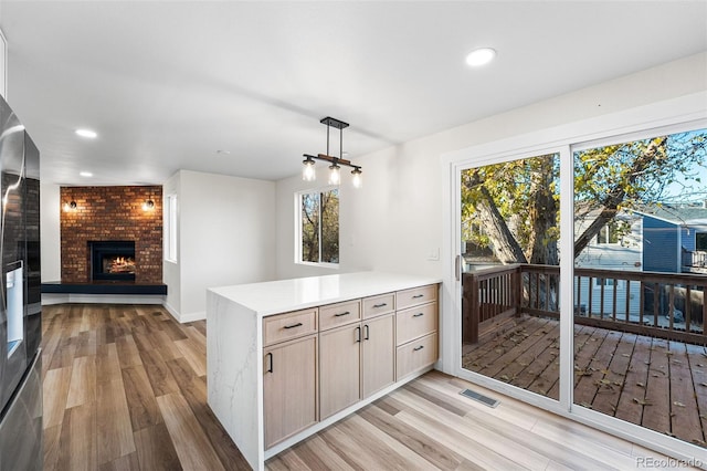 kitchen featuring light brown cabinets, kitchen peninsula, pendant lighting, a fireplace, and light wood-type flooring