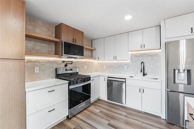 kitchen with sink, light hardwood / wood-style flooring, decorative backsplash, appliances with stainless steel finishes, and white cabinetry