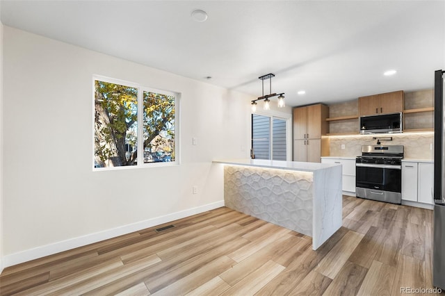 kitchen featuring white cabinetry, pendant lighting, light wood-type flooring, and appliances with stainless steel finishes