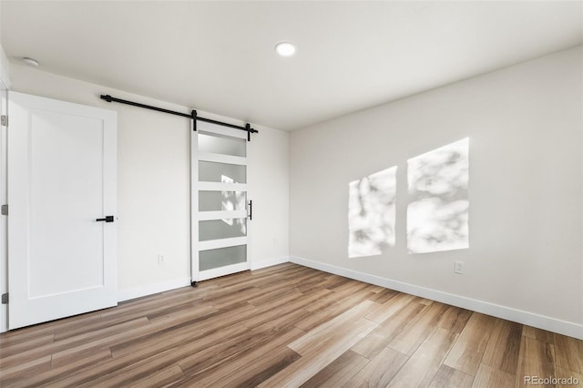 unfurnished bedroom featuring a barn door and light wood-type flooring