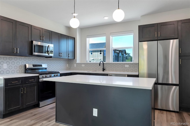 kitchen with a kitchen island, stainless steel appliances, backsplash, decorative light fixtures, and light wood-type flooring