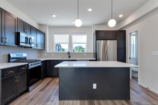 kitchen featuring pendant lighting, decorative backsplash, stainless steel appliances, and light wood-type flooring