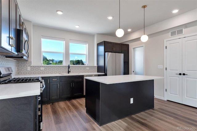 kitchen featuring hardwood / wood-style floors, tasteful backsplash, appliances with stainless steel finishes, pendant lighting, and a center island