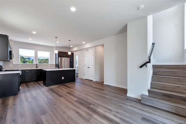 kitchen featuring tasteful backsplash, wood-type flooring, appliances with stainless steel finishes, a center island, and hanging light fixtures