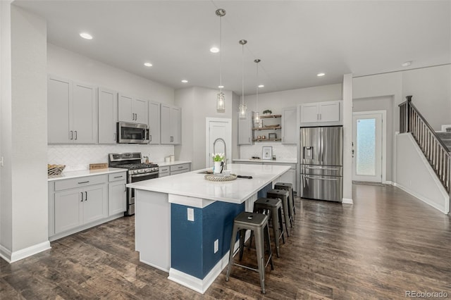 kitchen with a kitchen island with sink, stainless steel appliances, dark wood-type flooring, light countertops, and a kitchen bar