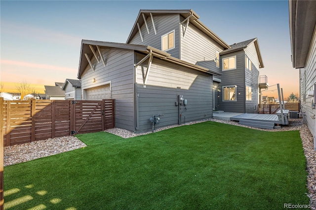 back of property at dusk with central AC unit, a garage, a fenced backyard, and a lawn