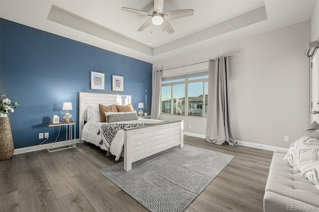 bedroom with baseboards, a raised ceiling, and wood finished floors