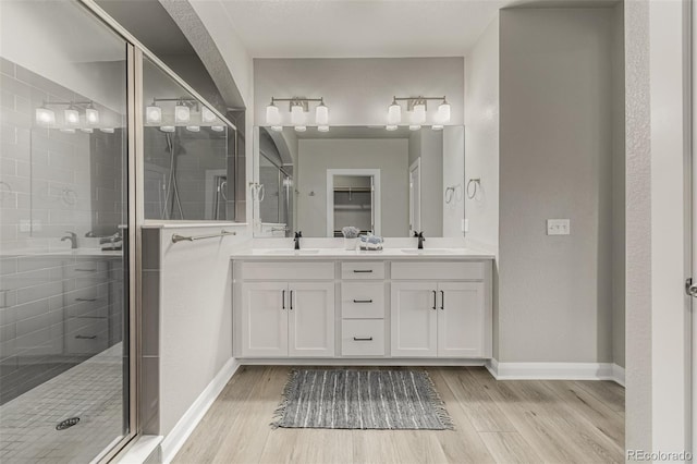 full bathroom with double vanity, wood finished floors, a stall shower, and a sink