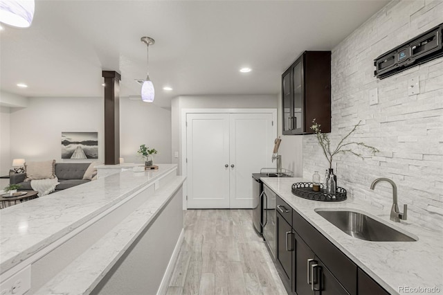 kitchen featuring light wood-type flooring, light stone counters, decorative backsplash, ornate columns, and a sink