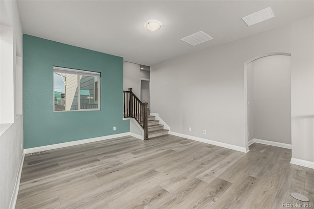 unfurnished room featuring stairway, wood finished floors, visible vents, and baseboards