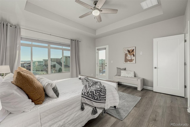 bedroom with visible vents, ceiling fan, baseboards, a tray ceiling, and wood finished floors