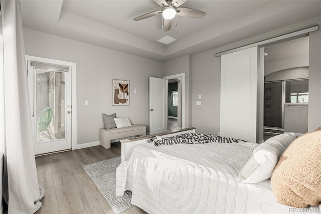 bedroom featuring access to exterior, baseboards, a tray ceiling, and wood finished floors