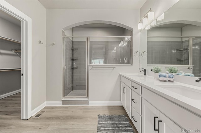 bathroom featuring visible vents, a sink, wood finished floors, a shower stall, and double vanity