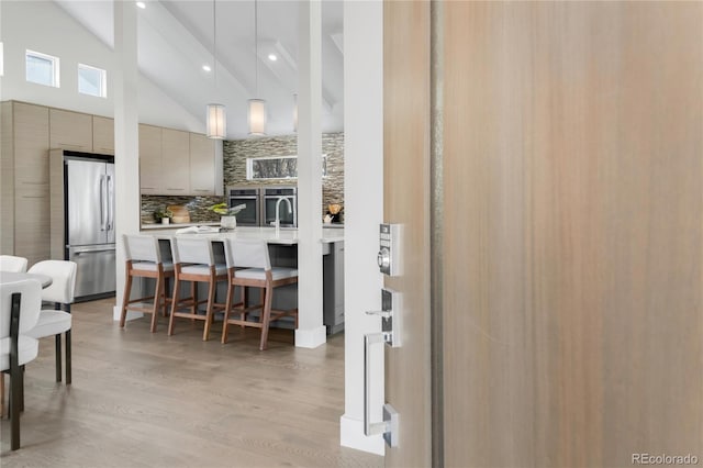 kitchen with a breakfast bar area, light countertops, decorative backsplash, modern cabinets, and stainless steel fridge