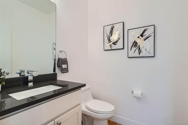 half bathroom featuring toilet, baseboards, and vanity