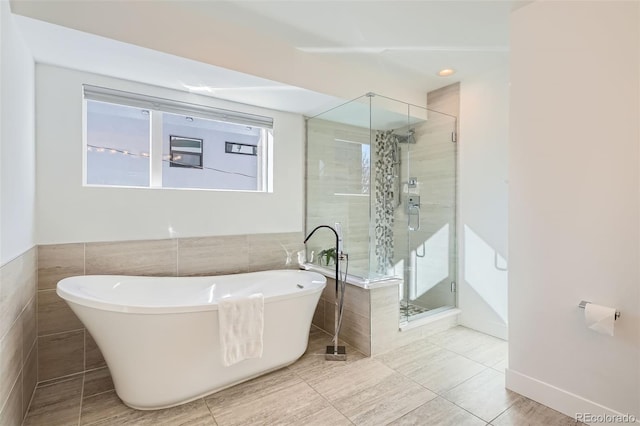 bathroom featuring a stall shower, a soaking tub, and tile walls