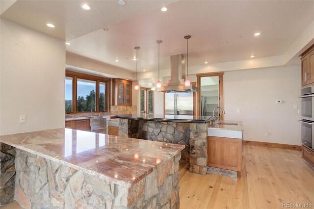 180 Outpost Ln, Evergreen, CO 80439 - kitchen featuring island range hood, a sink, light wood-style flooring, brown cabinets, and a peninsula