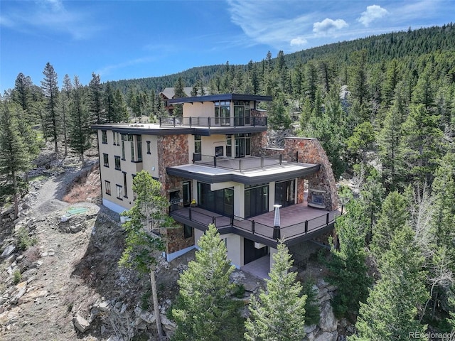 180 Outpost Ln, Evergreen, CO 80439 - rear view of property featuring a forest view, a balcony, stucco siding, and stone siding