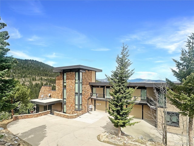 180 Outpost Ln, Evergreen, CO 80439 - view of front facade featuring driveway, a balcony, a garage, a mountain view, and stucco siding
